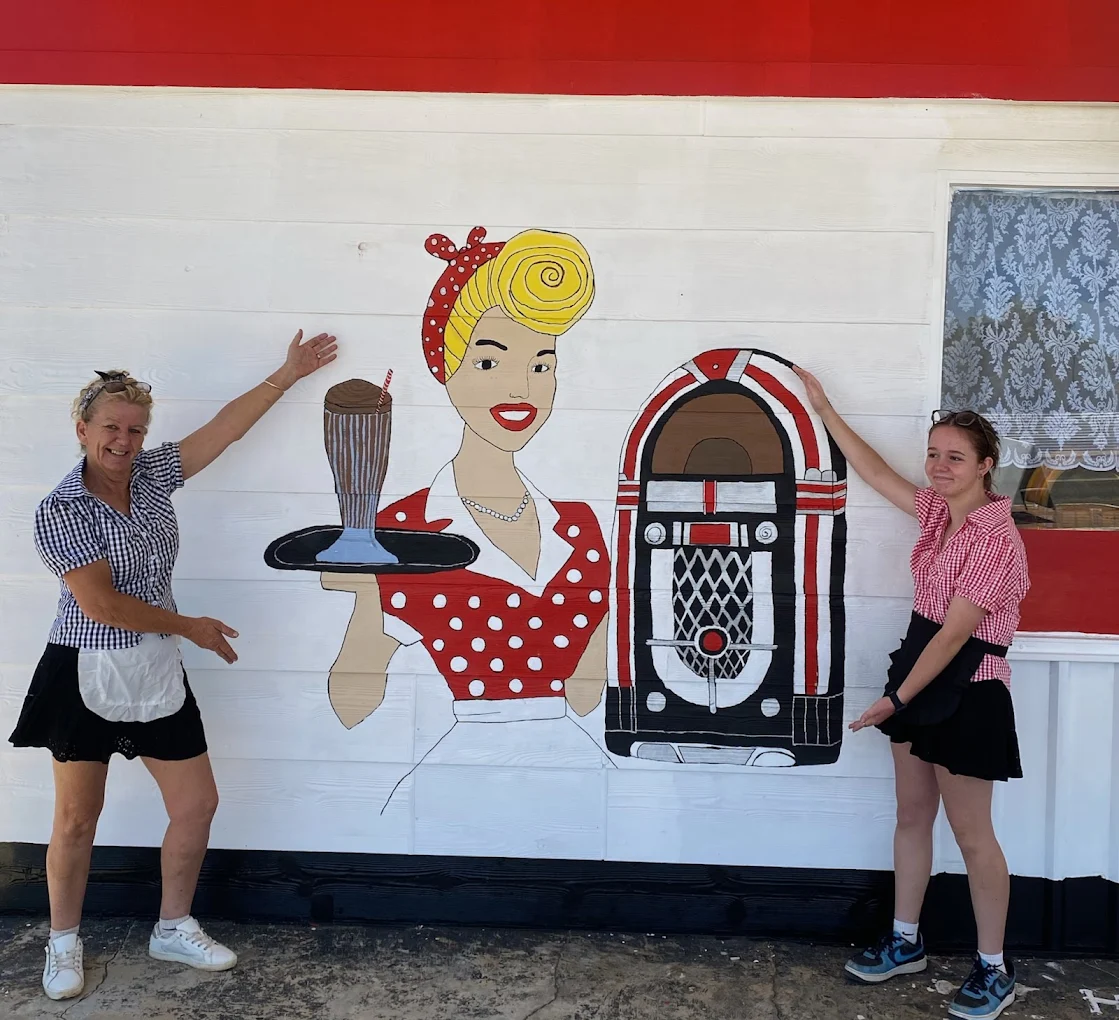 Two staff members posing in front of the retro mural at Somewhere to Go diner in Northampton WA